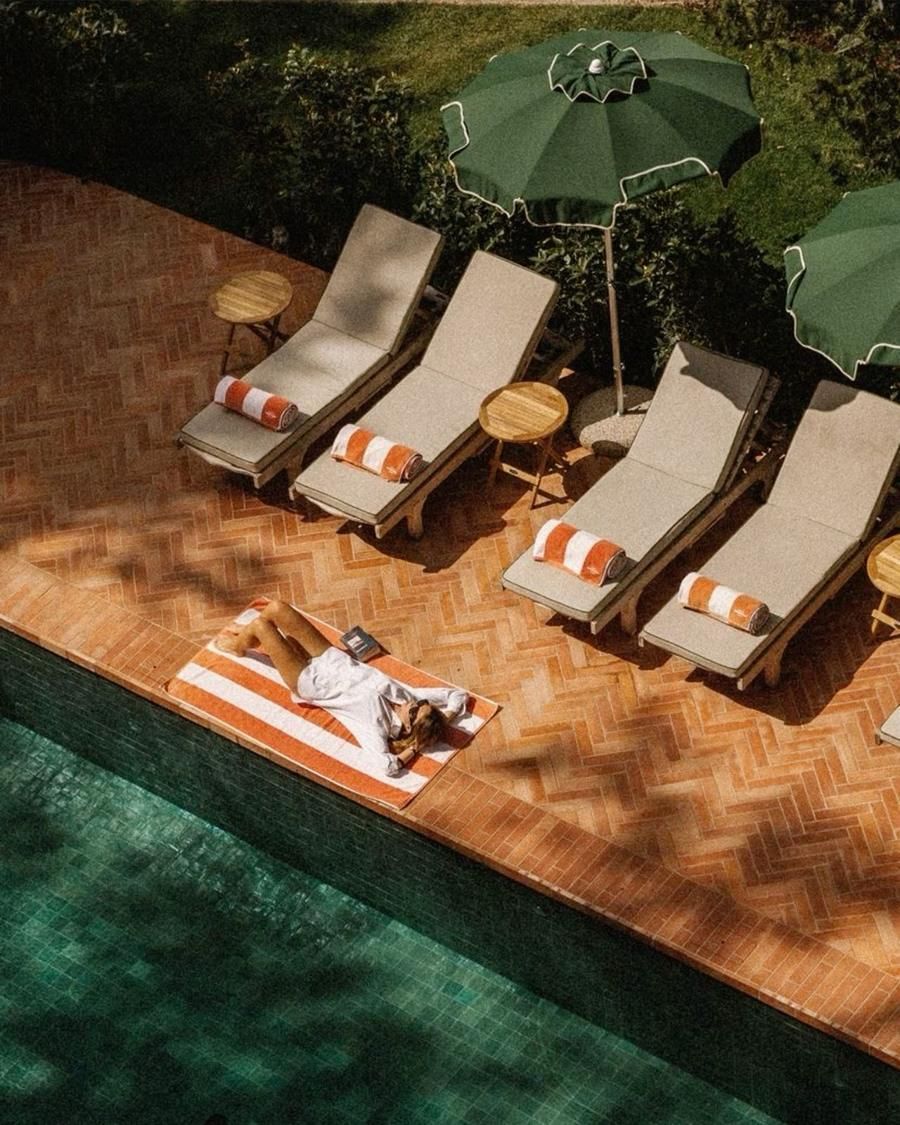 Guests beside a green-tiled hotel pool with striped towels and green parasols
